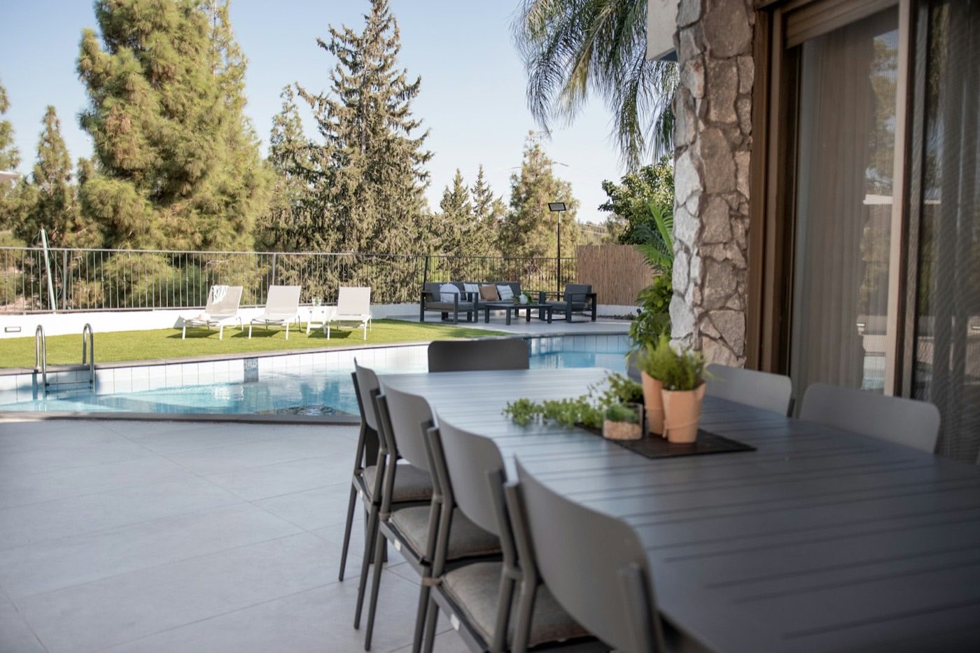 Outdoor dining table and chairs set on the deck beside a long pool.