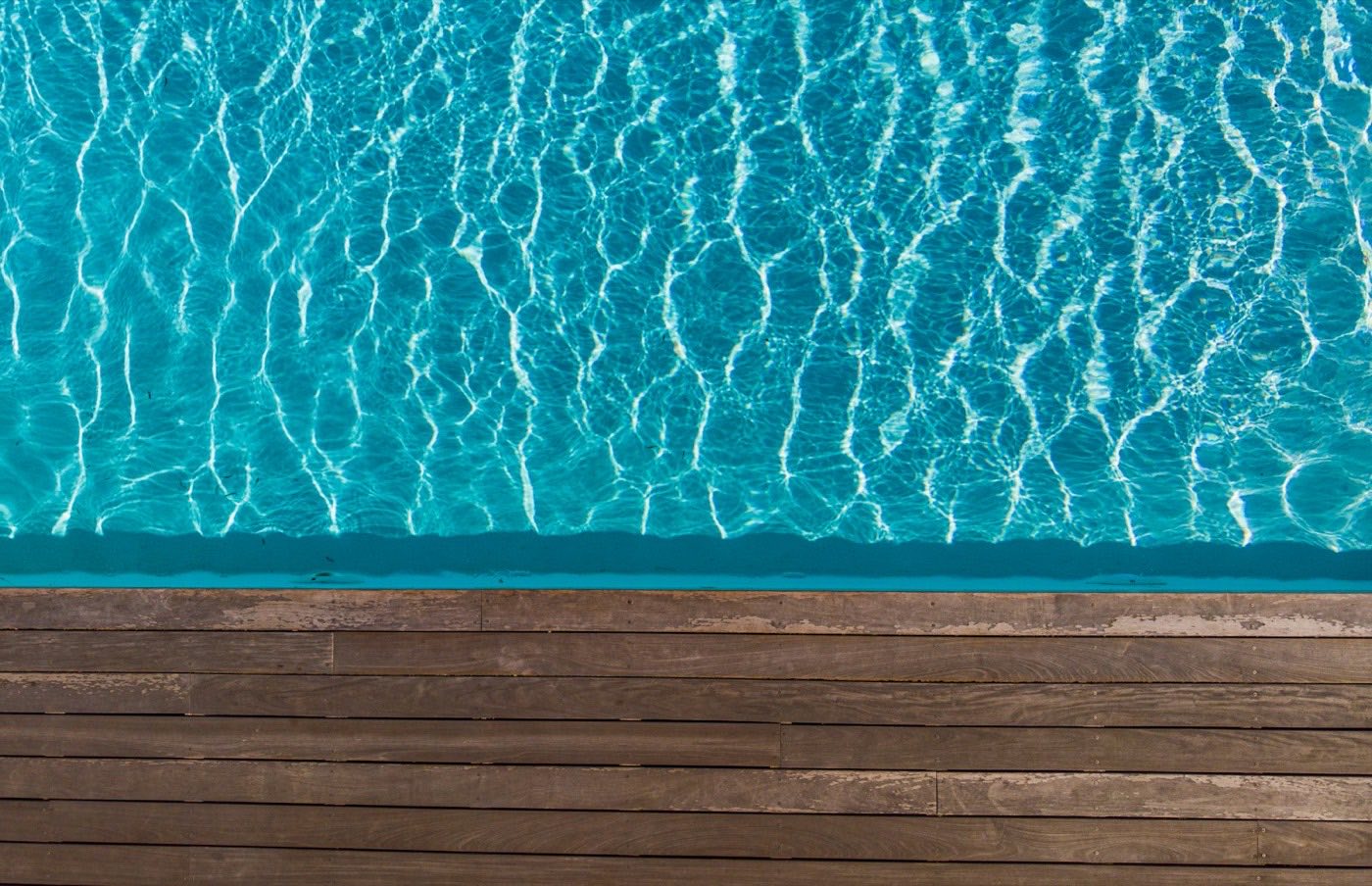 Sunlit pool water meeting the edge of a timber deck.