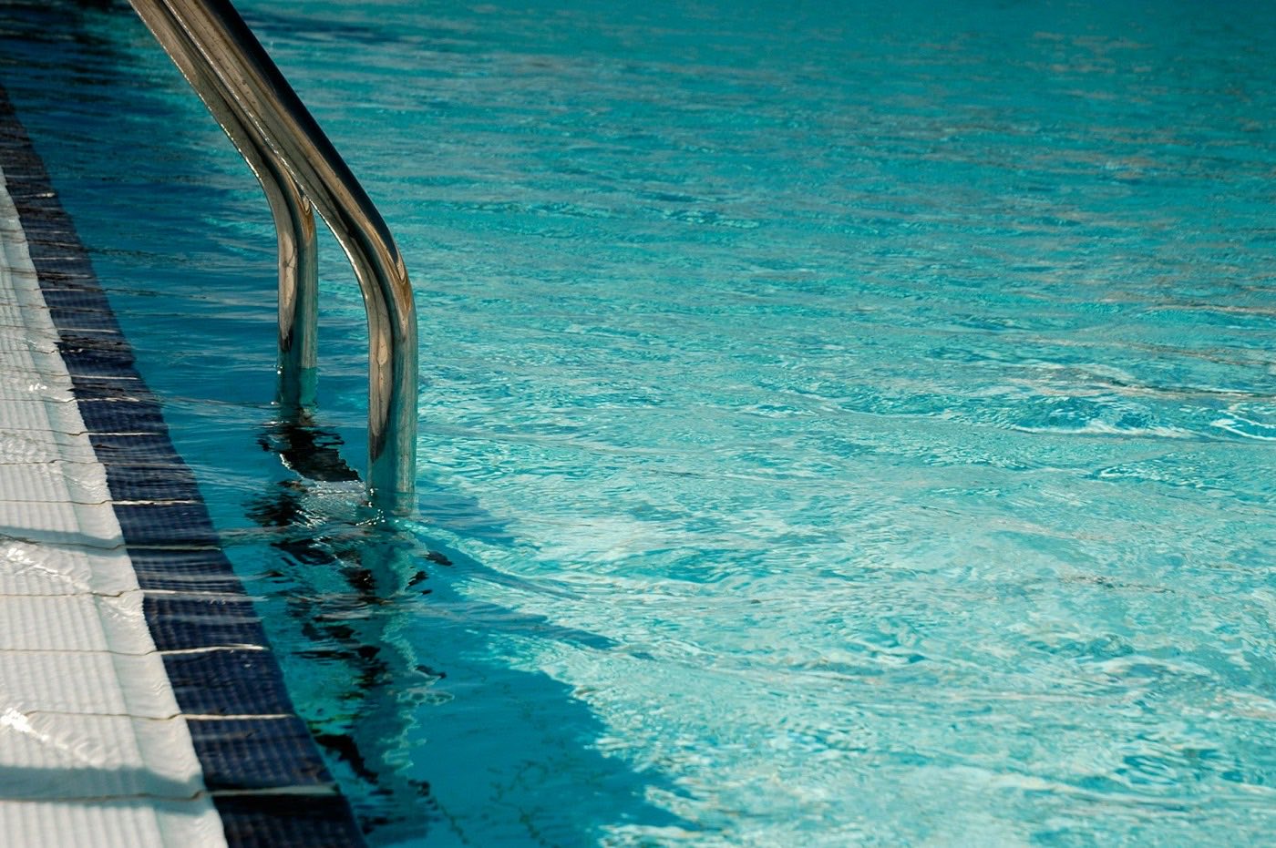Pool entry steps and handrail under clear blue water.