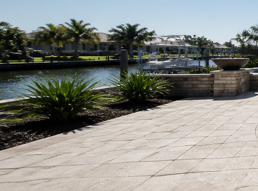 Waterfront pool deck with raised planters and a fire bowl overlooking a boat canal.