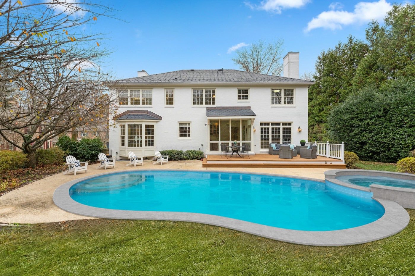 Kidney-shaped pool with an attached spa behind a white two-story home.